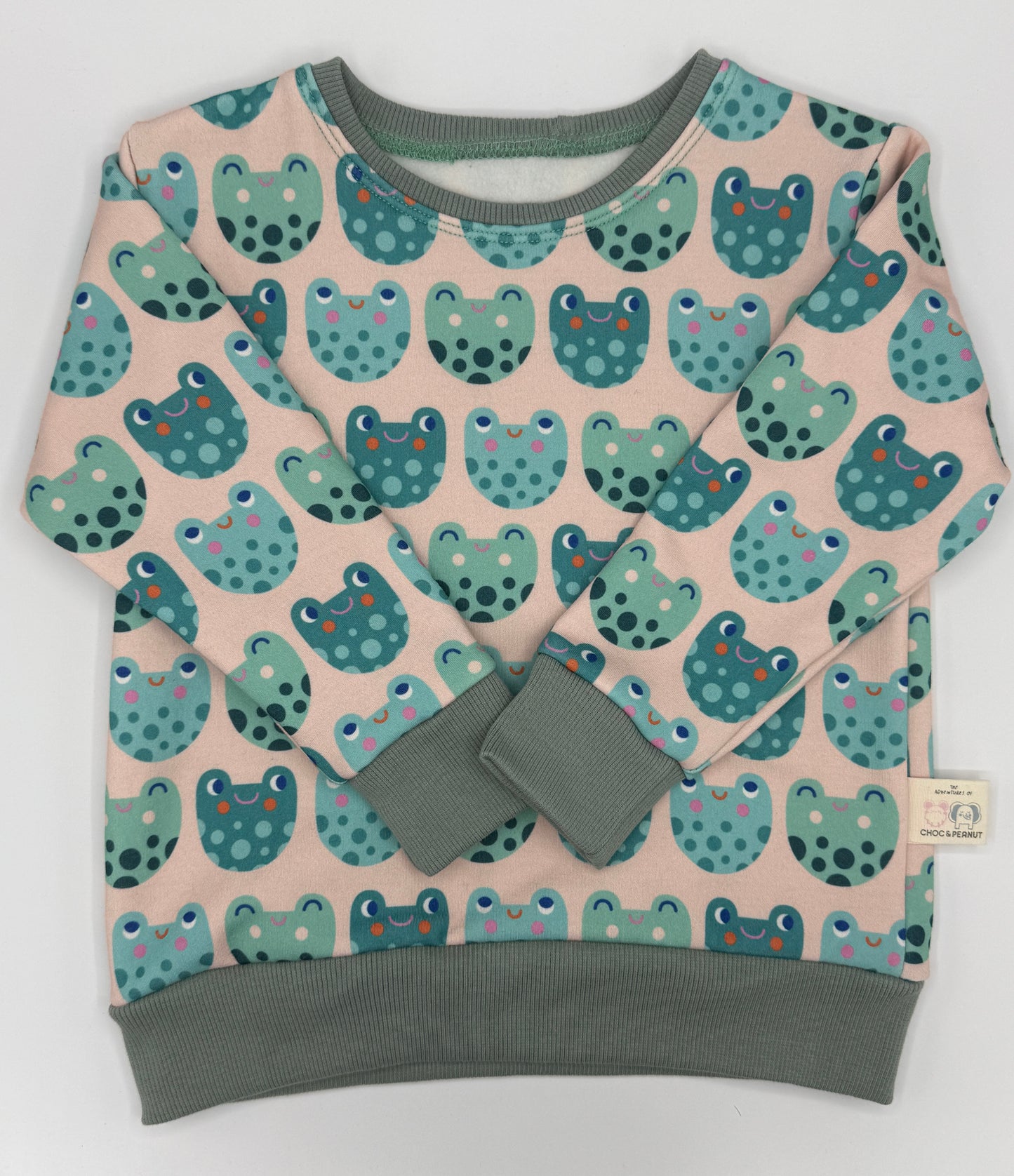 Frog detail unisex kids jumper made from sustainable fabric. Green frogs on pale pink background. 