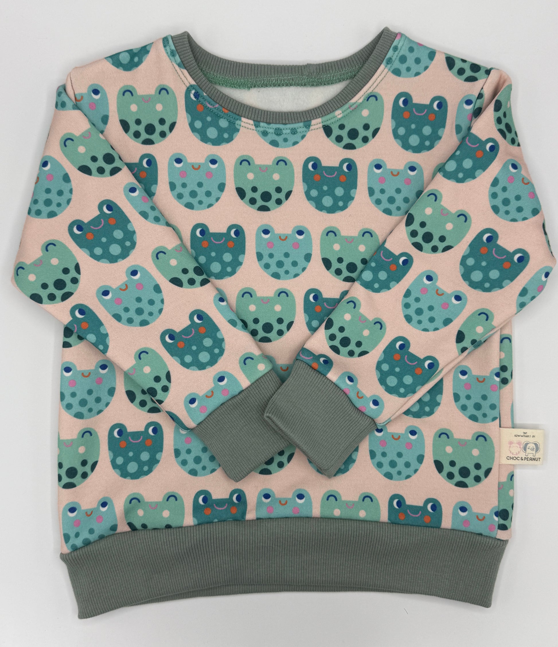 Frog detail unisex kids jumper made from sustainable fabric. Green frogs on pale pink background. 