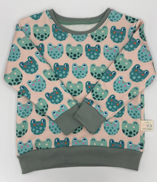 Frog detail unisex kids jumper made from sustainable fabric. Green frogs on pale pink background. 