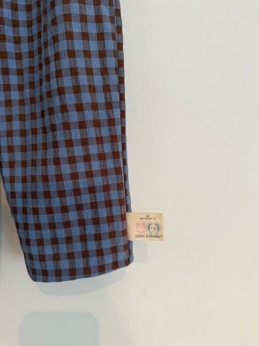 A close-up of a blue and brown gingham 100% cotton Seersucker patterned fabric kids trousers with an elasticated waist and hand sewn hem. Organic 